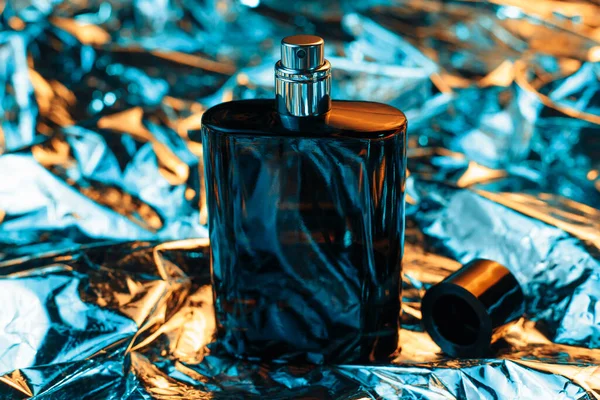 Black bottle of men perfume in neon lights on the foil with shiny crumpled surface background. 80s and 90s style.
