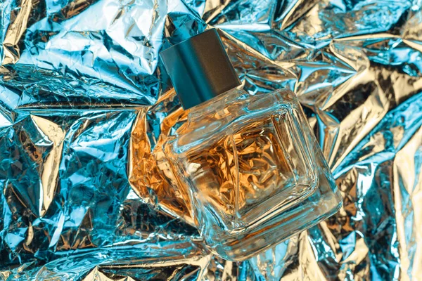 Stylowa butelka kobiecych perfum w neonowych światłach na folii z błyszczącym pogniecionym tłem powierzchni. Lata 80-te i 90-te. — Zdjęcie stockowe
