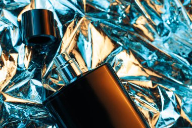 Siyah erkek parfümü şişesi folyodaki parlak, buruşuk yüzey arkaplanlı neon ışıklarıyla. 80 'ler ve 90' lar tarzı.