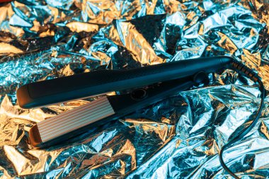 Folyoda parlak buruşuk yüzey arkaplanlı, neon ışıklı saç düzleştirici. 80 'ler ve 90' lar tarzı.