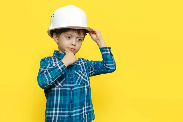 穿着防护头盔的小男孩工程师或建筑师，带着黄色背景的建筑计划. — 图库照片