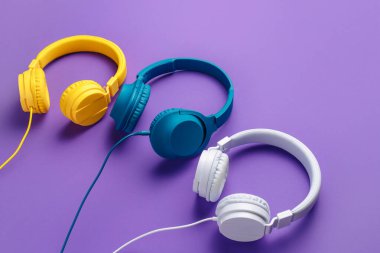 Mor arka planda üç kulaklık. Müzik konsepti.
