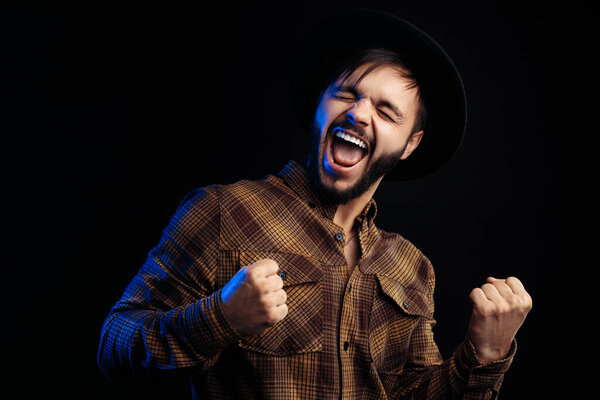 Excited young bearded hipster in brown shirt over black background.