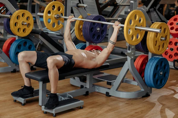 Confiado atlético joven culturista fitness modelo pecho de ejercicio con barra en el banco en el gimnasio. —  Fotos de Stock