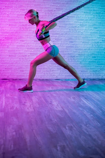 Entrenamiento de mujer rubia joven con bandas elásticas en el gimnasio con luces de neón. — Foto de Stock