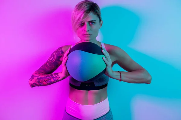 Přizpůsobit mladé blondýny žena cvičení s medicínou míč v tělocvičně v neon světla. — Stock fotografie
