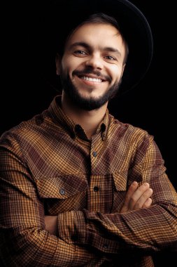 Kahverengi gömlekli mutlu genç sakallı hippi siyah arka planda gülümsüyor..