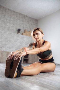 Spor elbiseli çekici sarışın, zayıf kadın spor salonunda esneme hareketleri yapıyor..