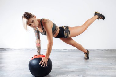 Spor salonunda tıp topuyla egzersiz yapan zinde sarışın bir kadın..