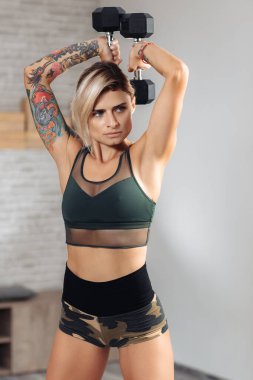 Spor salonunda trisepsler için halter egzersizi yapan atletik sarışın kadın..