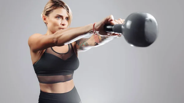 Fit young blonde woman workout in the studio with Cettlebell over gray background. — стоковое фото