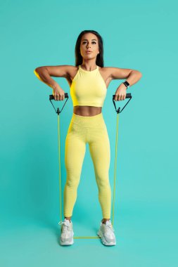 Mavi arka planda uzun bantlı omuzlarını çalıştıran uzun boylu genç bir kadının fotoğrafı..