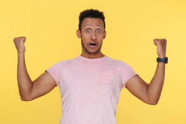 Başarılı Afrikalı Amerikalı genç adam ellerini sarı arka planda tutarak bağırıyor..