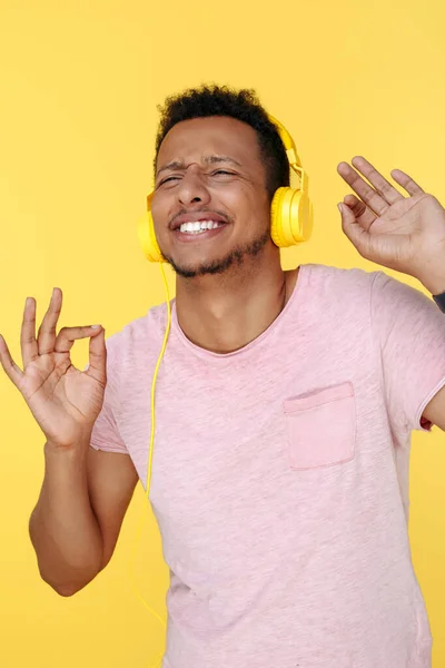 Grappig Afrikaans Amerikaans jongeman luisteren muziek in koptelefoon en dansen over gele achtergrond. — Stockfoto