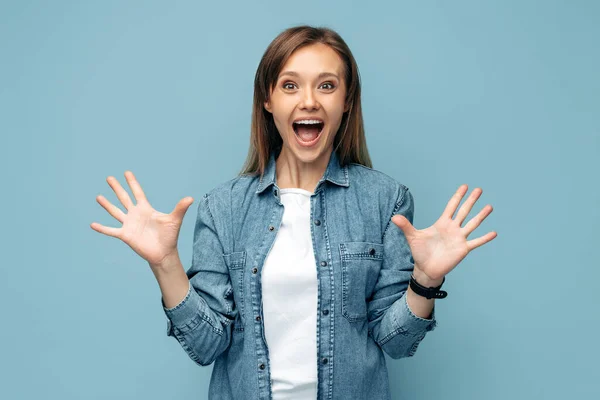 Opgewonden jonge vrouw in jeans shirt vieren succes schreeuwen over blauwe achtergrond. Kijk in de camera.. — Stockfoto