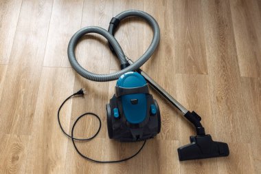 Oturma odasındaki ahşap zeminde modern mavi elektrikli süpürge. Kalp Şekli. Temiz Ev Konsepti.