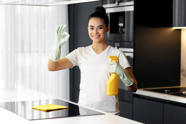 Mutfakta sprey kullanırken ev işlerini yapan neşeli bir kadın. Genç bayan iyi bir hareket gösteriyor..