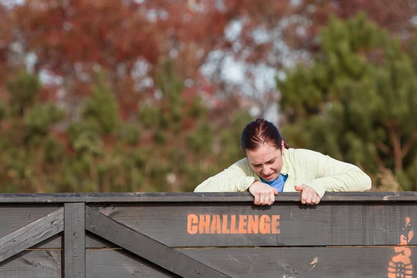 Kvinnan kämpar dra sig över muren på hinderbana Race — Stockfoto