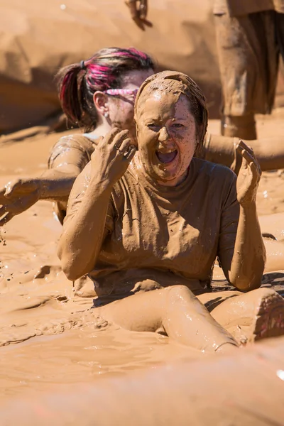 Мутная женщина сидит и смеется над девушкой, бегущей по грязи — стоковое фото