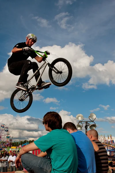 BMX jezdec provádí kousek nad třemi posluchačů na veletrhu — Stock fotografie