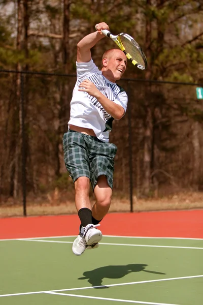 Jugador de tenis masculino sigue a través de saltar por encima de tiro — Foto de Stock