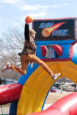 Teen Soars Above Rim To Dunk Basketball In Carnival Game clipart