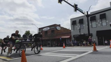 Lawrenceville, GA / USA - 20 Nisan 2024: Yavaş çekim ekibi, 20 Nisan 2024 'te Lawrenceville, GA' da evsizler için yerel bir bağış toplama etkinliğinde, tekerlekli sandalyeler üzerinde ev yapımı bir yatağı aşağı itiyor..