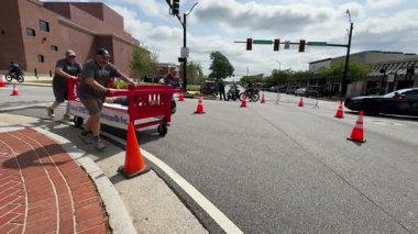 Lawrenceville, GA / USA - 20 Nisan 2024: Yavaş çekim ekibi, 20 Nisan 2024 'te Lawrenceville, GA' da evsizler için yerel bir bağış toplama etkinliğinde, tekerlekli sandalyeler üzerinde ev yapımı bir yatağı aşağı itiyor..