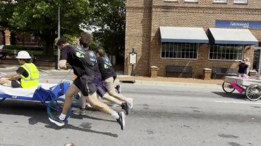 Lawrenceville, GA / USA - 26 Nisan 2025: Ağır çekim, 26 Nisan 2025 'te Lawrenceville, GA' da evsizler için yerel bir bağış toplama etkinliğinde iki takımın tekerlekli sandalyeler üzerinde ev yapımı yatakları ittiğini gösteriyor..