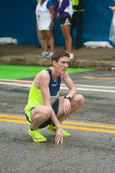 Utmattade löpare knäböjer för att fånga andan vid Peachtree Road Race — Stockfoto