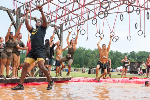 Los competidores se balancean de los anillos sobre el agua en carrera de obstáculos extremos — Foto de Stock