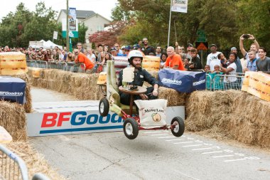 Man Steers Furniture Vehicle Over Ramp In Soap Box Derby clipart