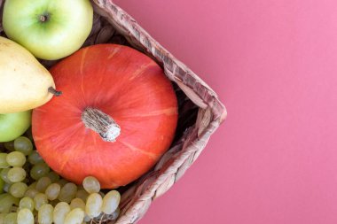 Sepet pembe arka planda meyvelerle dolu. Doğal organik balkabağı, elma, armut ve üzüm. Üst görünüm.