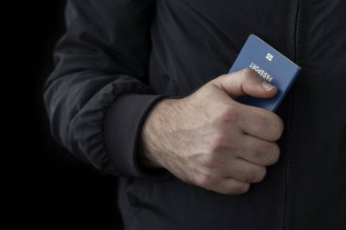 Passport in male hand on black background. Illegal migration concept. clipart