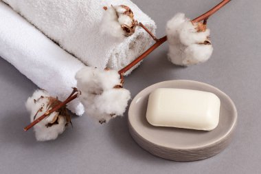 Gri arkaplanda beyaz havlular, sabun ve pamuk dalı.