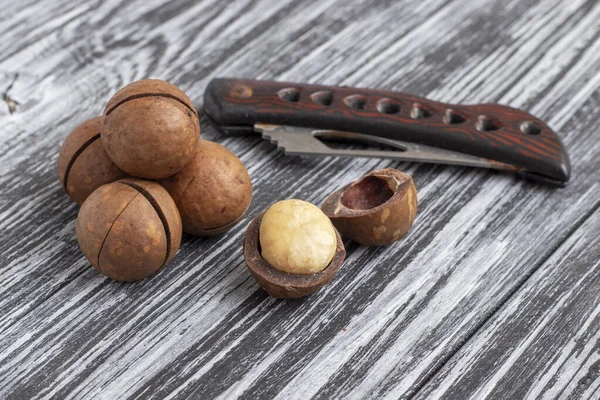 Macadamia nuts and a knife to stab nuts on black wooden table.