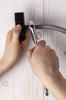 Kadın tesisatçı esnek hortumu siyah su durdurucusuna bağlıyor. Beyaz ahşap arka planda.