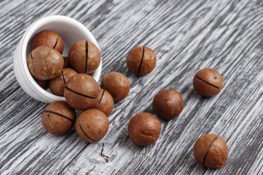 Siyah ahşap masada küçük beyaz kasede Macadamia fındıkları..
