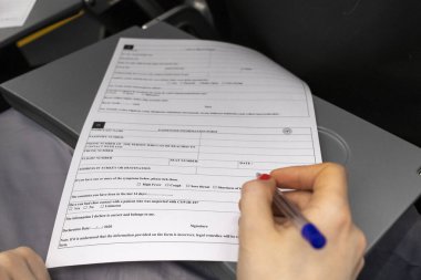 İSTANBUL, Turkey - 4 HAZİRAN 2021. Uçakta bir kadın yolcu bilgilendirme formu dolduruyor. Yolcunun son zamanlarda Covid-19 hastalarıyla görüşüp görüşmediğini sorgula.