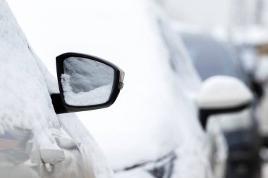 Açık otoparkta karla kaplı bir araba. Kanat aynası karla kaplı..