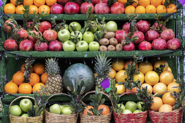 гранаты, апельсины, яблоки и другие фрукты на полках уличного фруктового магазина.