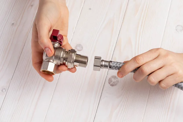 Female plumber connecting flexible hose to stopcock. On white wooden background.