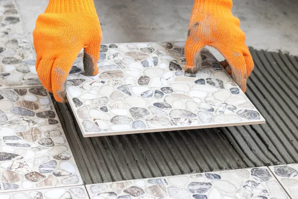 İşçi elleri bir fayansı tutar ve yere yapıştırıcı sürerek yerleştirir. Seramik seramik döşeme işlemi. Kapat..