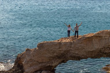 Aşık bir çift, deniz arka planındaki kayalık sahilde özgürlüğün tadını çıkarıyor..