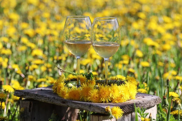 Wine glasses with yellow dandelion wine on an old wooden chair in the field.