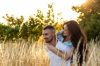 Gün batımında tarlada aşık romantik, şehvetli genç bir çift. Arkaplan ışığı, mercek parlaması.