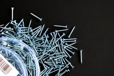 İnşaat bağlayıcıları. Kendi kendine dokunan vidalar karanlık bir arka planda düzensiz bir yığının içine saçılmış. İnşaat işçileri için mükemmel bir tasarım..