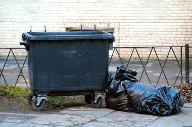 Tekerlekli çöp konteynırı. Yakınlara plastik bir çöp torbası atılmış. Ticari temizlik şirketi kavramı