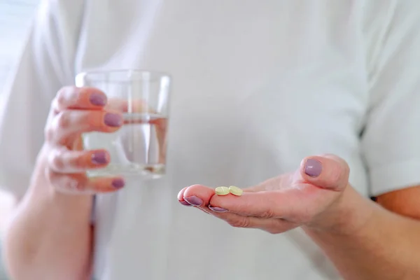 Close - up of a pill in one hand. The woman is going to wash down the medicine, holding a glass of water in her hand. Medicine concept medicines for stomach, sleep, digestion, headache medicine