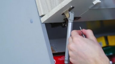 Mutfak mobilyalarının tamiri. Gevşek vidayı elektrikli tornavidayla bükmek..
